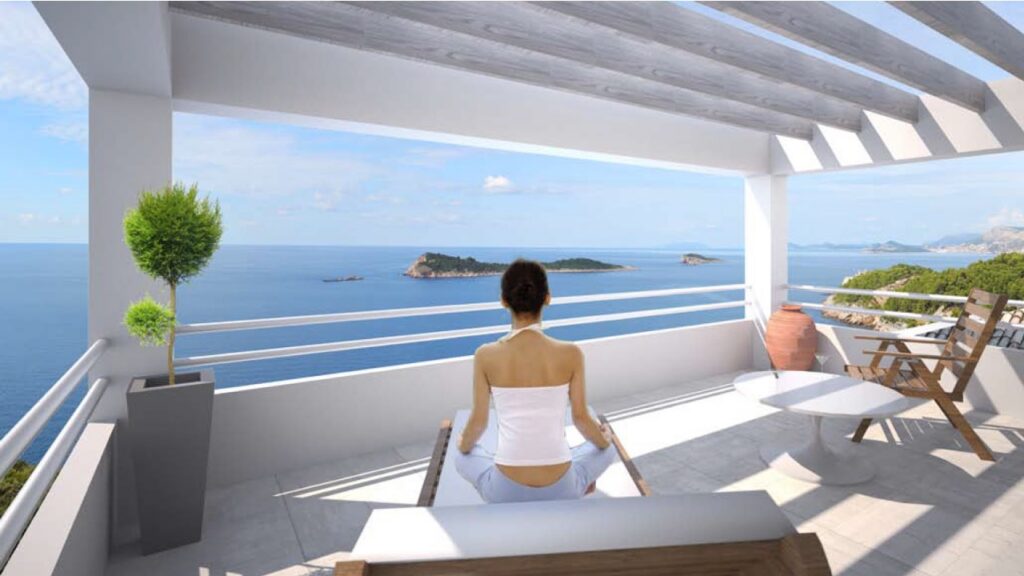 Dame som sitter på terrassen og ser utover havet.